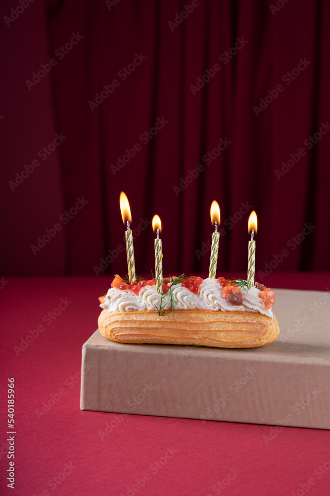 Salted eclair with candles on vinious background. Copy space. vertical. Postcard concept Salted eclair with candles on vinious background. Copy space. vertical. Postcard concept