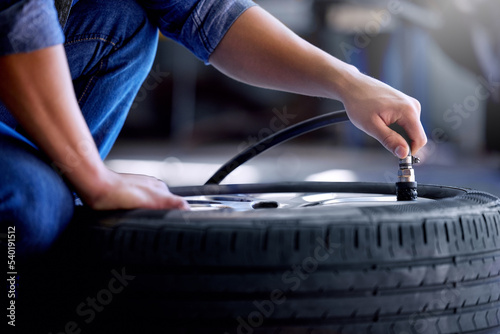 Air pressure, tire and mechanic working in garage with pump in hand. Man in auto service, vehicle care and checking car wheel in workshop. Technician doing maintenance check in motor repair industry