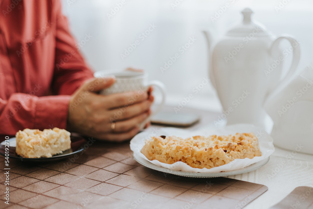 middle-aged woman sitting at the table in the cosy kitchen in the apartment and drinking tea with apple pie, cozy autumn days