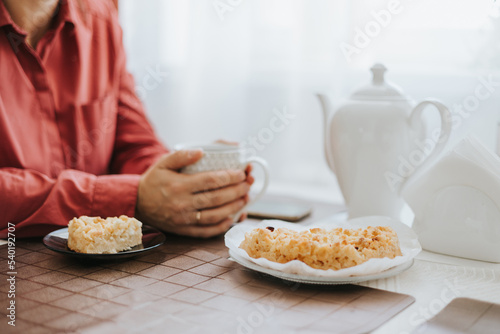 middle-aged woman sitting at the table in the cosy kitchen in the apartment and drinking tea with apple pie, cozy autumn days