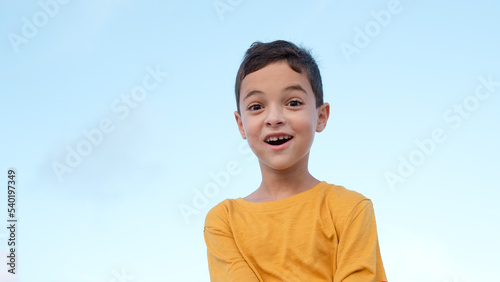 Cheerful positive child, blue sky on the background. Surprised face of a boy 8 years old. Emotion, facial expression, holidays, funny kid face, idea concept. Isolated. Brunette person, caucasian.