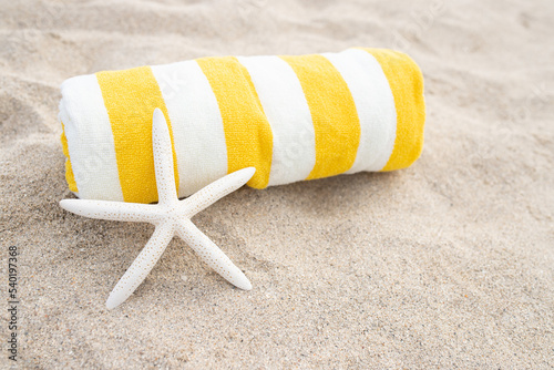 Rolled up striped white and yellow towel, white starfish shell on the sandy beach. Sunny day. The concept of tanning, vacation, relaxation, retreat, vacation, travel, sunbathing. Copy space. photo