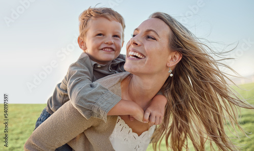 Mother, child and happy piggyback in summer, holiday and blue sky, sunshine and play in a green park. Happy mother, kid and smile having fun outdoor for vacation with smile, laugh and love in nature photo