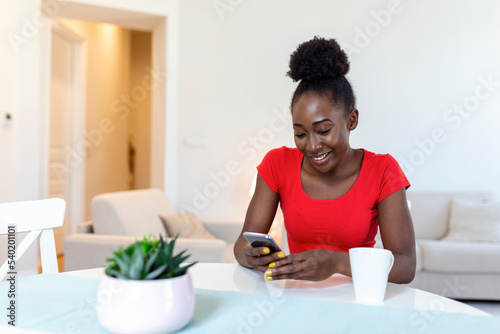 Young african american woman drinking coffee and chatting with friends at social network with her mobile phone