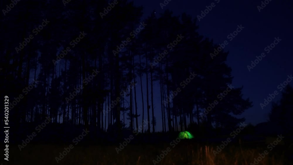 Light green tent glowing in the dark not far from the fading fire Light green tent glowing in the dark not far from the fading fire