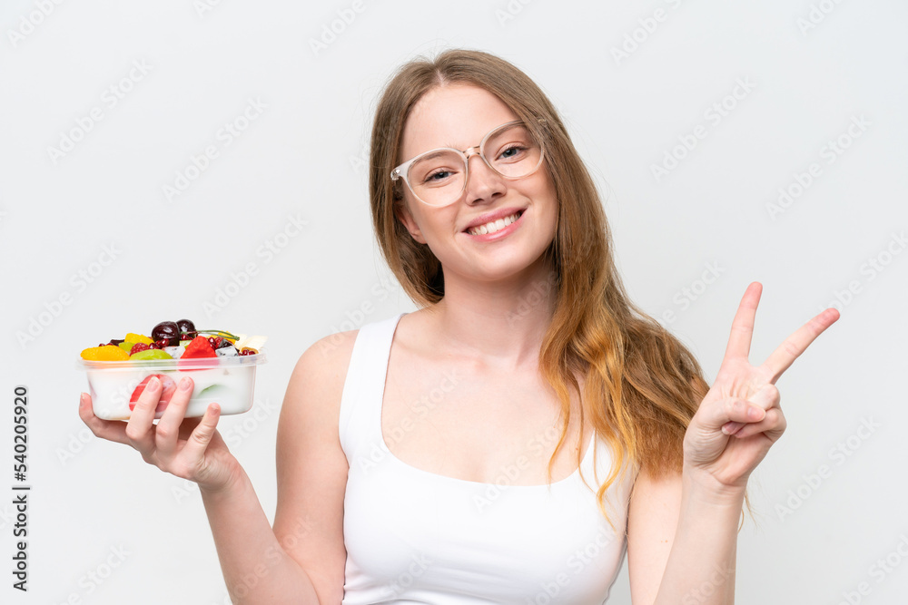 Young pretty woman holding a bowl of fruit isolated on white background smiling and showing victory sign Young pretty woman holding a bowl of fruit isolated on white background smiling and showing victory sign