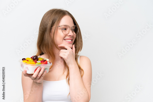 Young pretty woman holding a bowl of fruit isolated on white background thinking an idea and looking side