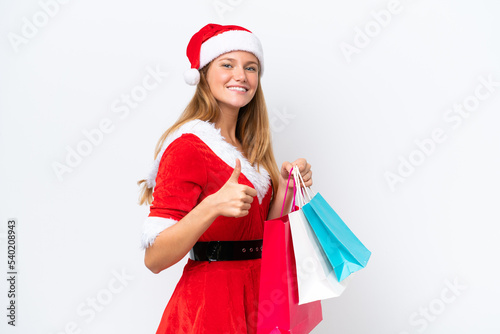 Young caucasian woman dressed as mama noel isolated on white background holding shopping bags and with thumb up