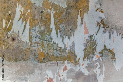 Old dilapidated wall with pieces of paper wallpaper and layers of multi-colored plaster. Architectural vintage texture with scratches and abrasions on the surface