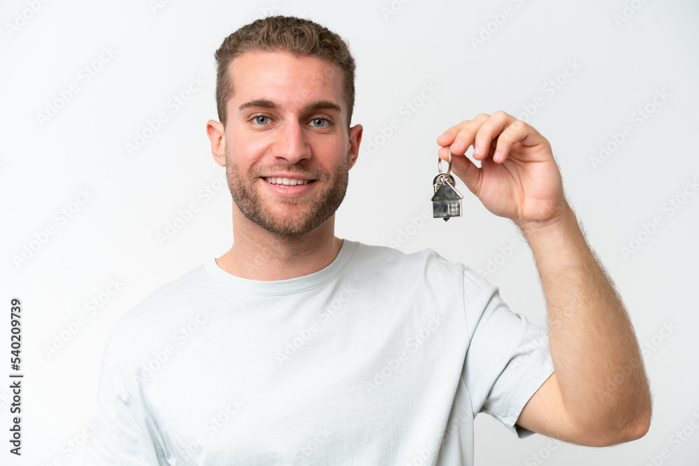 Young caucasian man holding home keys isolated on white background smiling a lot Young caucasian man holding home keys isolated on white background smiling a lot