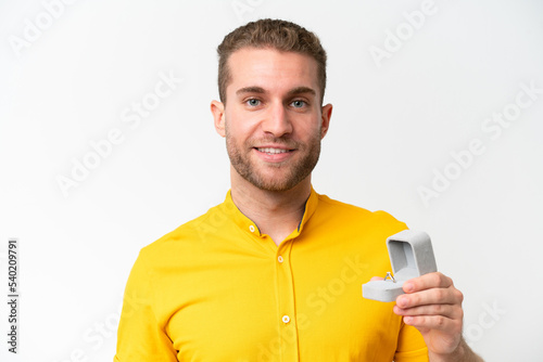Young man holding a engagement ring isolated on white background smiling a lot