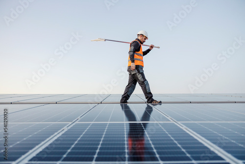 Worker with broom on his shoulder is walking on the roof with solar panels.