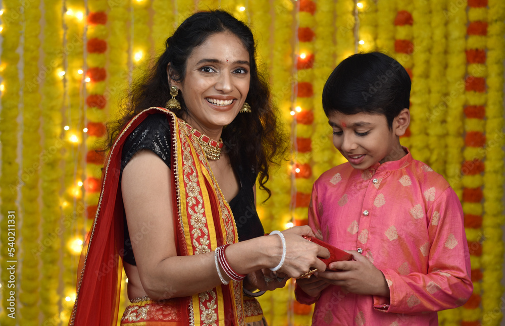 Young woman and son celebrating diwali,holding plate of diyas, gift boxes 