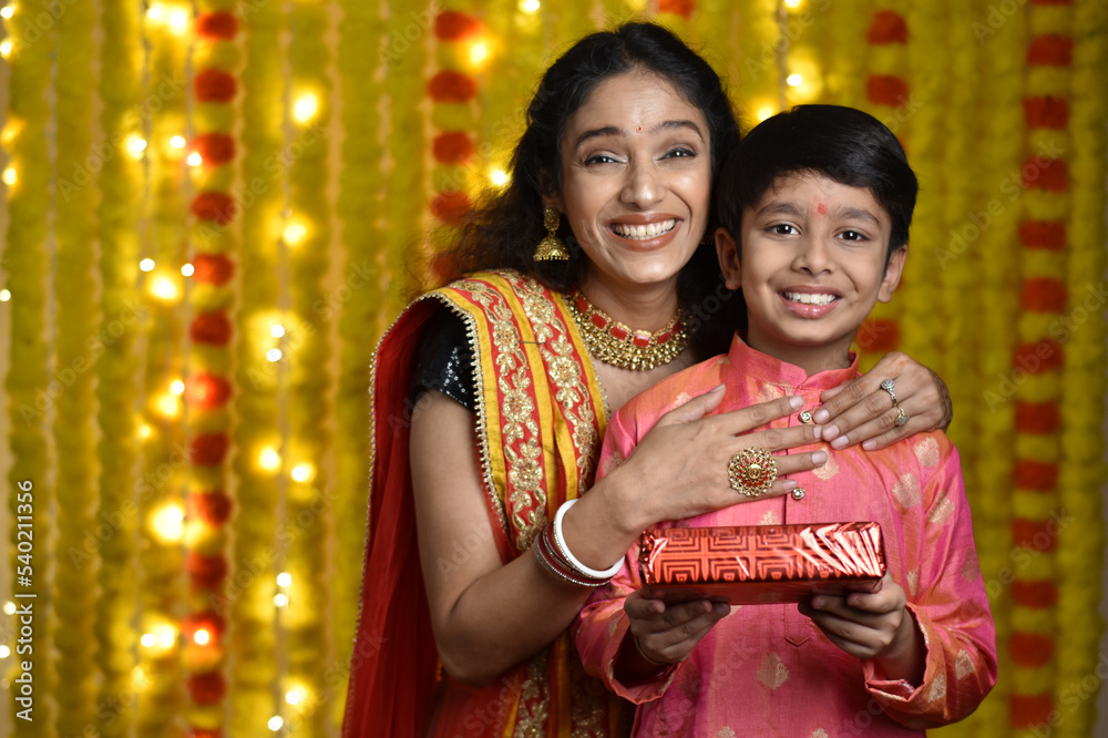 Young woman and son celebrating diwali,holding plate of diyas, gift boxes Young woman and son celebrating diwali,holding plate of diyas, gift boxes