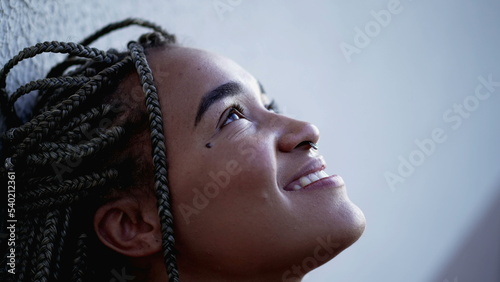 A hopeful Brazilian young woman looking up to sky with HOPE and FAITH. Spiritual contemplative female person closeup face feeling free