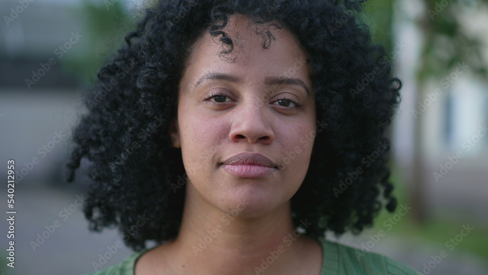 One young black woman looking at camera closeup face portrait standing outdoors with serious expression. Natural casual beauty with curly hair One young black woman looking at camera closeup face portrait standing outdoors with serious expression. Natural casual beauty with curly hair