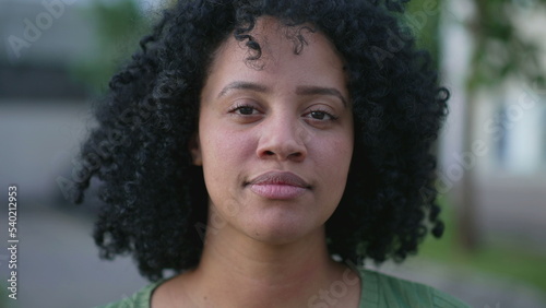 One young black woman looking at camera closeup face portrait standing outdoors with serious expression. Natural casual beauty with curly hair © Marco