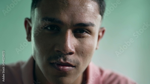 Portrait of a hispanic young man closeup face with serious expression looking at camera. One young Brazilian South American person
