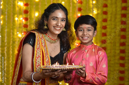 Happy young woman and son celebrating diwali holding plate of diyas,gift boxes