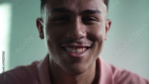 One happy hispanic young man closeup face. Portrait of a South American Brazilian male person looking at camera smiling indoors