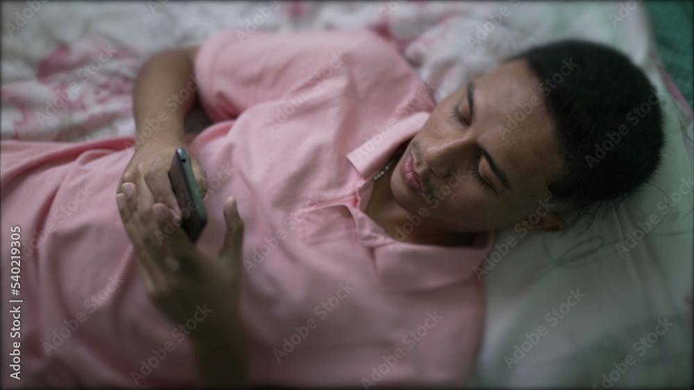 One hispanic man lying in bed using smartphone. A South American young person looking at phone screen One hispanic man lying in bed using smartphone. A South American young person looking at phone screen