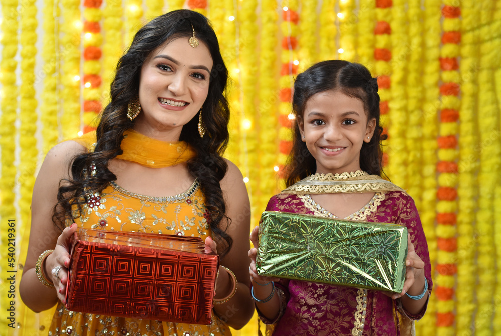Happy young woman and daughter celebrating diwali holding gift boxes 