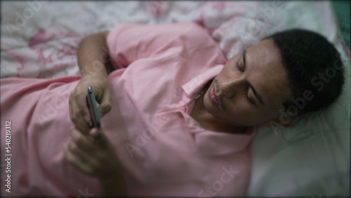 One hispanic man lying in bed using smartphone. A South American young person looking at phone screen