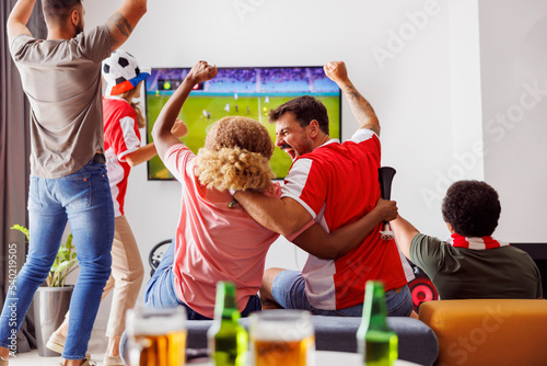 Friends cheering while watching football on TV © Impact Photography
