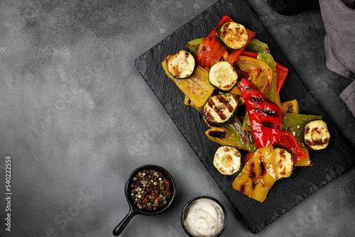 Grilled vegetable, bell sweet pepper and zucchini with sauce on a black slate board and dark background. Healthy vegan food. Top view, copy space.