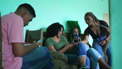 Female friend sharing cellphone screen to group of girlfriends at home. Candid group of hispanic black friends together