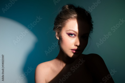 Creative close-up portrait of a beautiful girl with eyeliner standing on stage with a beam of bright light