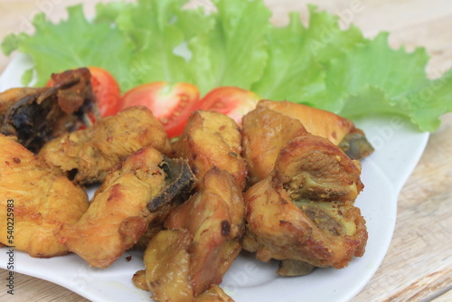 Fried chicken on a white plate with lettuce and tomato slices on a wooden table