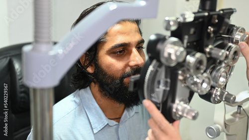 Indian male patient checking eye vision with phoropter eyesight measurement testing machine. ye health check and ophthalmology concept