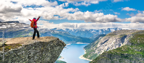Hiker woman stands at rock and looks at aerial view in the mountains. Amazing nature view on the way to Trolltunga. Location: Scandinavian Mountains, Norway, Odda. The feeling of complete freedom