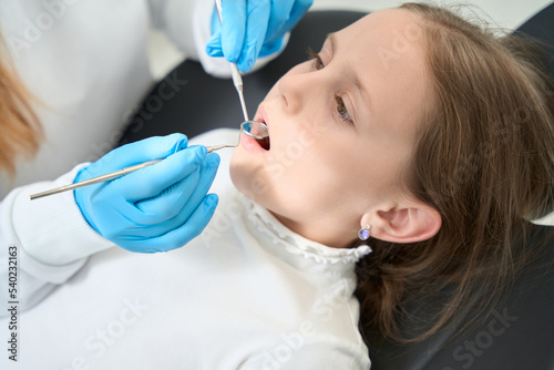 Professional pediatric dentist examining teeth of little girl