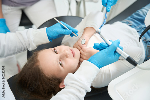 Pedodontist treating little patient teeth assisted by nurse