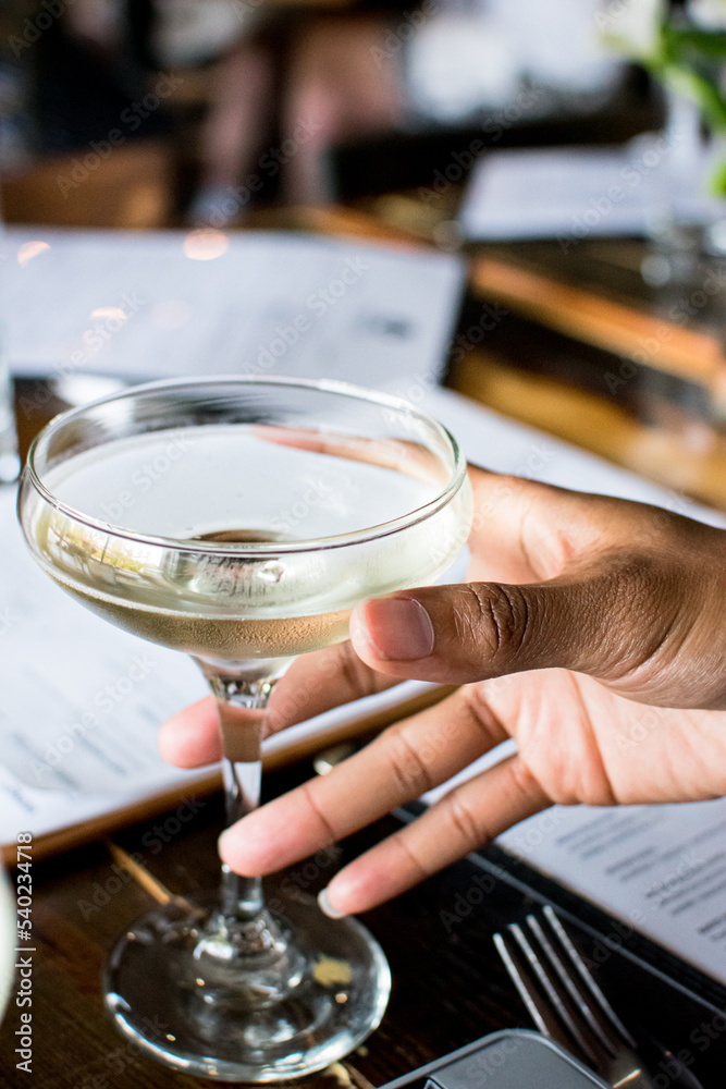 Black woman hand holding a coupe cocktail glass at a restaurant 