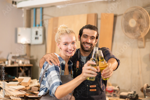 Happy couple carpenter drinking after work finish together in wood workshop