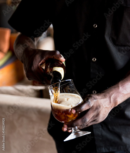 Black man, African man waiter hand pouring beer into a glass at a restaurant in Rwanda 