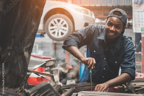 African man mechanic in uniform with tools and wrenches standing at the car repair station