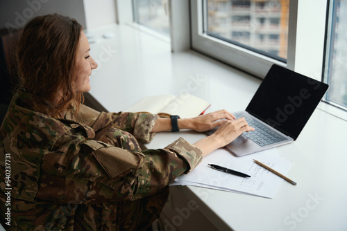 Military woman typing on laptop keyboard and making notes