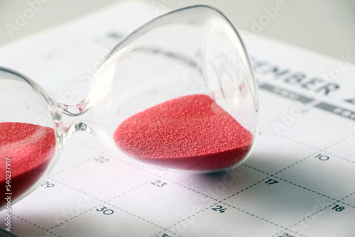 Red sand in hourglass, on its side, fallen on calendar, signifying time out, pause in time, taking a break, need for more time photo