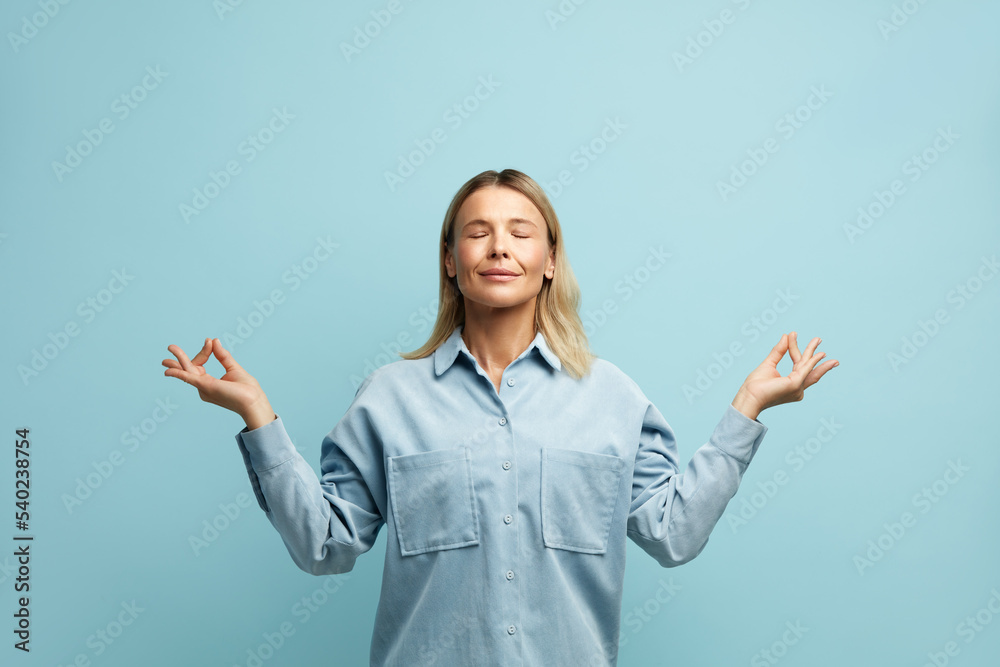 Peaceful Woman Meditating at Studio. Portrait of Attractive Young Girl Relaxing and Doing Meditation Gesture with Fingers, Practicing Yoga. Indoor Studio Shot Isolated on Blue Background Peaceful Woman Meditating at Studio. Portrait of Attractive Young Girl Relaxing and Doing Meditation Gesture with Fingers, Practicing Yoga. Indoor Studio Shot Isolated on Blue Background