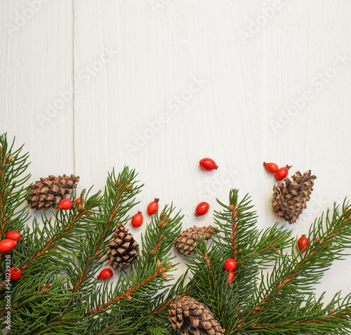  Spruce, fir branches, cones, red berries on white wooden background. Frame border. Christmas New Year composition background. Space for text.