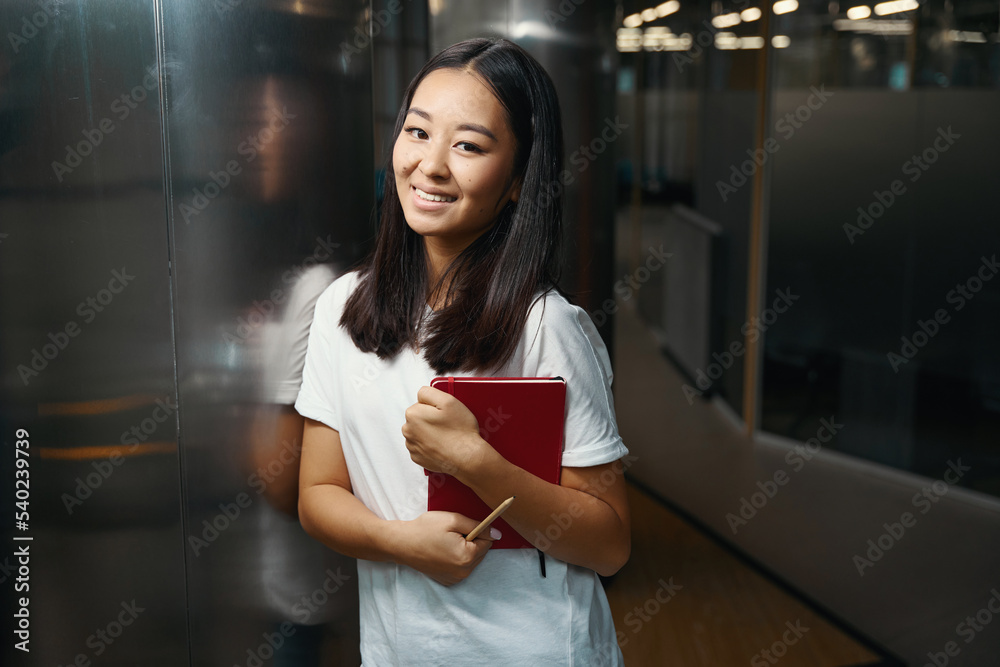 Happy cheerful Asian woman standing near the glass door and posing