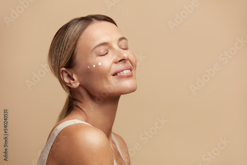 Woman Cream Drops On Face. Portrait Of Woman Closed Eyes With Cosmetic Cream On Skin Under Eyes. Closeup Of Beautiful Female With Beauty Product On Soft Skin, Natural Makeup 