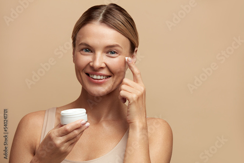 Beauty Woman Applying Face Cream. Closeup Of Female Model With Fresh Skin Holding Cream Bottle In Hand. Portrait Of Sexy Girl Applying Cosmetic Product Under Eyes. Skincare Concept. High Resolution 