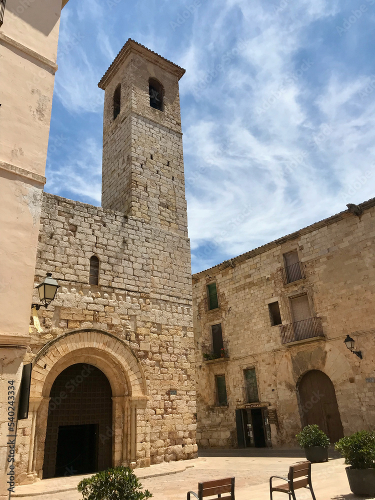 Montblanc, Spain, June 2019 - A stone church with a clock tower in front of a brick building