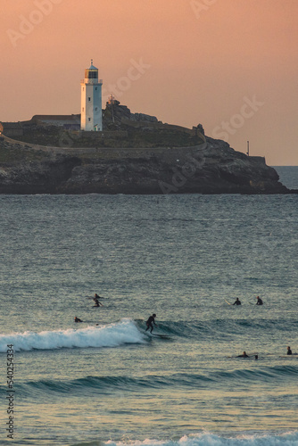 surfer riding wave in front of godrevy lighthouse