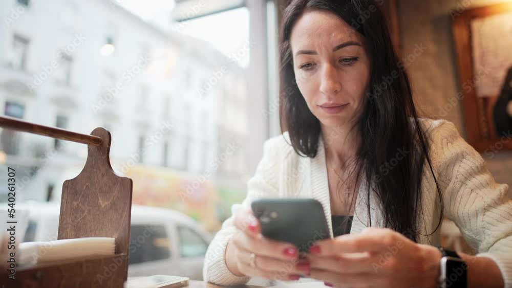 Portrait young beautiful businesswoman sitting in cafe or restaurant, holds in hands and using mobile phone for typing message or reading news. Remote work or online communication in cozy coffee shop. Portrait young beautiful businesswoman sitting in cafe or restaurant, holds in hands and using mobile phone for typing message or reading news. Remote work or online communication in cozy coffee shop.